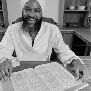 A black and white photo of a man with a turban sitting at a desk.