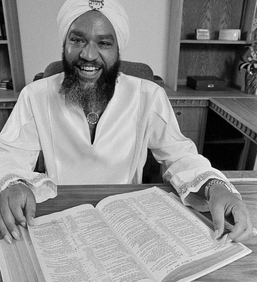 A black and white photo of a man with a turban sitting at a desk.